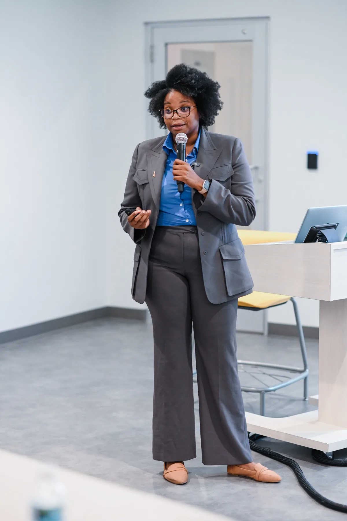Dr. Maya Byfield presenting to a room, holding a microphone and a slide clicker