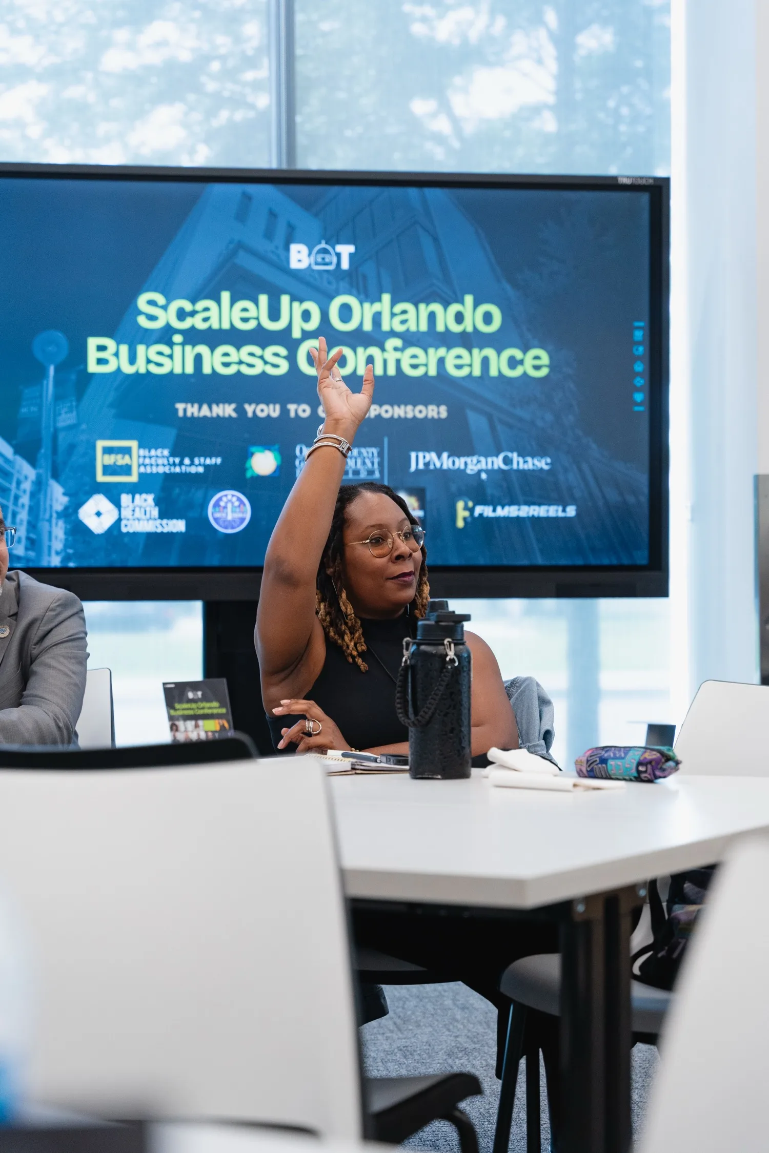 A participant raising her hand at the ScaleUp Orlando Business Conference, in front of a screen crediting BOT&rsquo;s sponsors