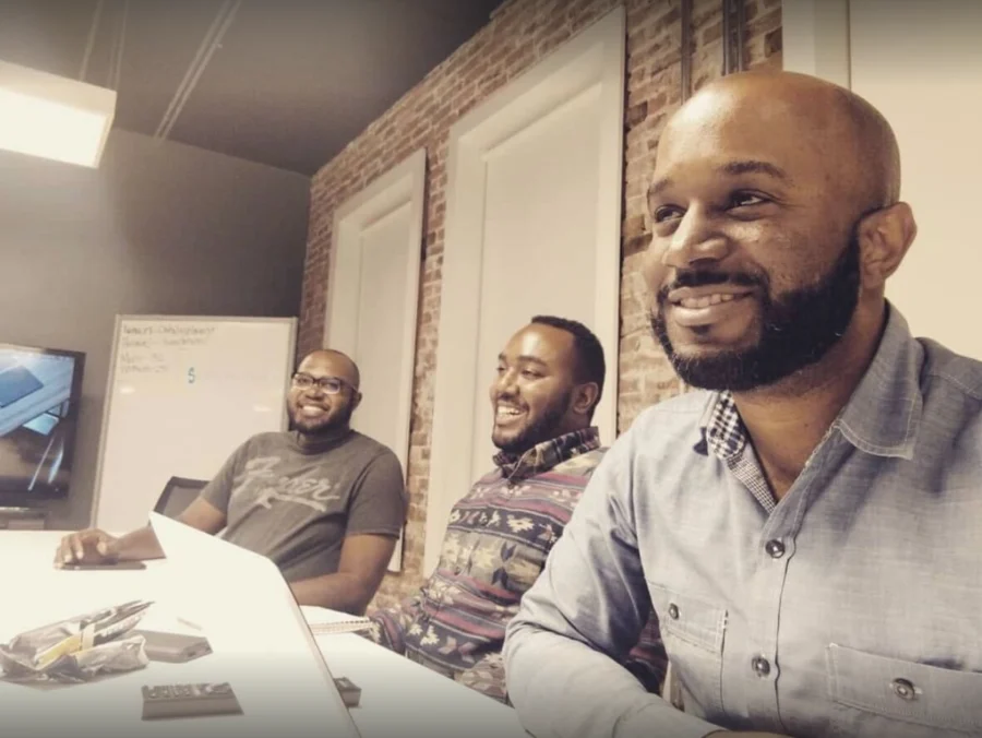 Three of Building Our Tech&rsquo;s earliest members around a table at Catalyst Co-Working Space, mid-laugh during the first town-hall meeting