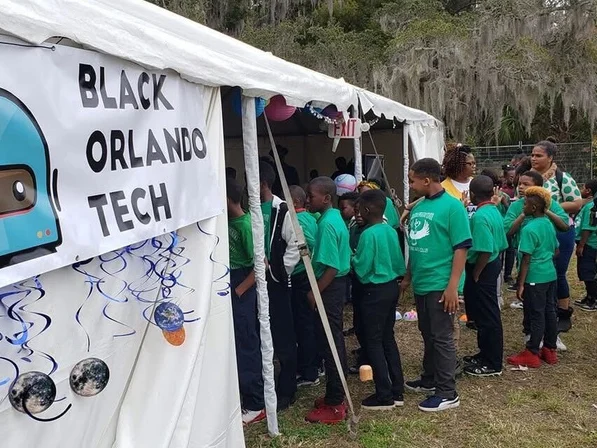 Children in matching green shirts lined up beside a Black Orlando Tech banner at the Zora Neale Hurston Festival