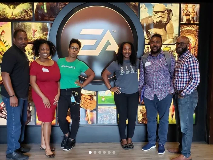 Members standing in front of an illuminated EA Sports sign during a studio visit