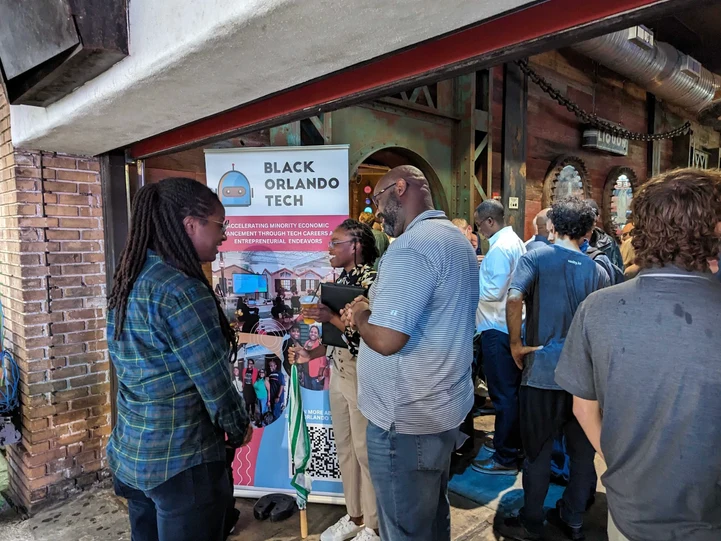 Attendees gathered around a Black Orlando Tech pop-up banner at the entrance to a brick-walled venue during TenX Tech Con