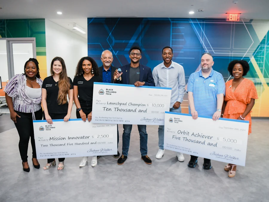 Nine people standing together holding three oversized Building Our Tech cheques &mdash; ten thousand, five thousand and two thousand five hundred dollars &mdash; at the Launchpad Liftoff Pitch Competition